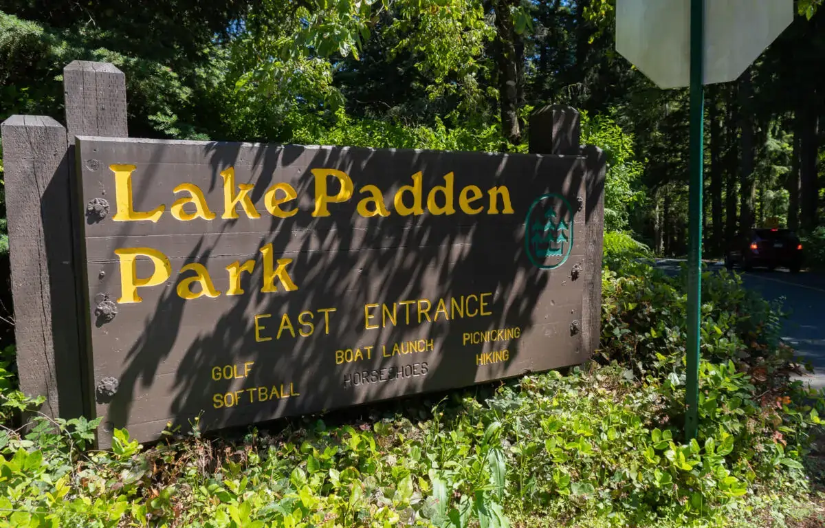 Entrance sign for Lake Padden Park East Entrance surrounded by trees and greenery, listing activities such as golf, softball, boat launch, horseshoes, picnicking, and hiking., dog-park